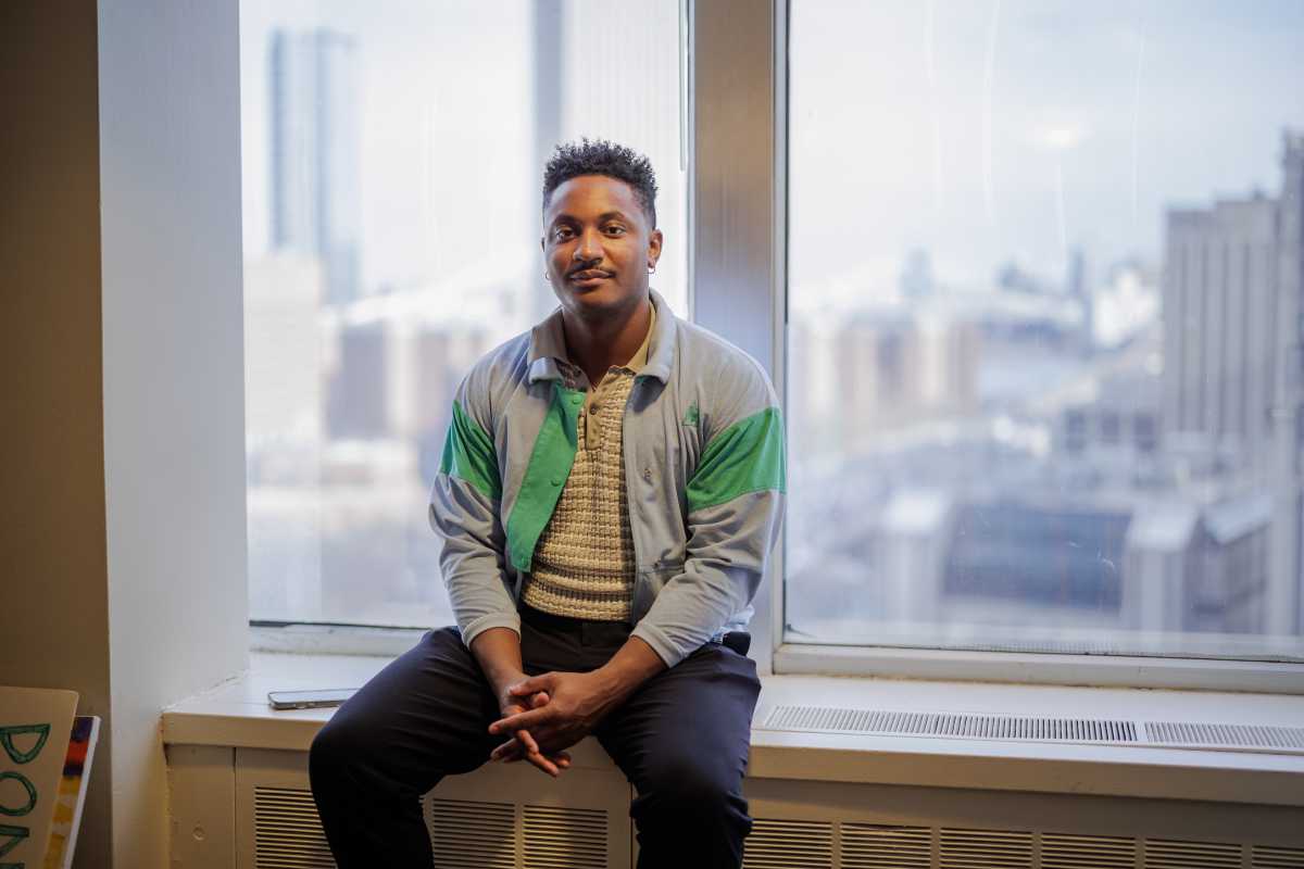 council member chi ossé sitting on the window sill in his office in a green and blue jacket